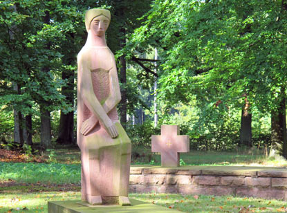 Diese sitzende Skulptur erinnert an die Gefallenen des 2. Weltkriegs. Um das Denkmal stehen auf einer kleinen Mauer 7 Sandsteinkreuze.